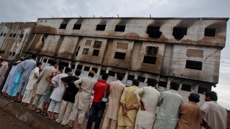 Жители стоят у швейной фабрики, которая загорелась накануне, в Карачи, 13 сентября 2012 года.