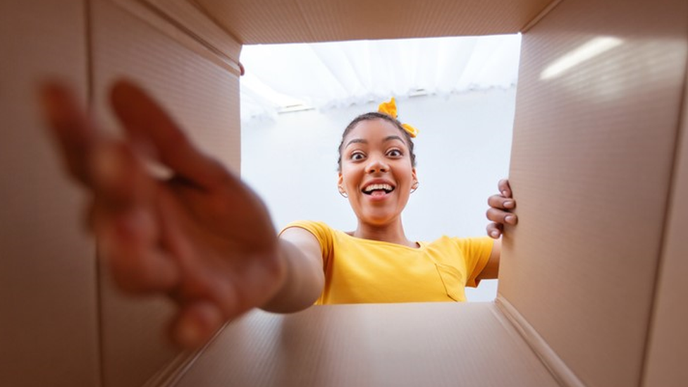 Foto tirada de dentro da caixa mostra mulher sorrindo ao receber presente