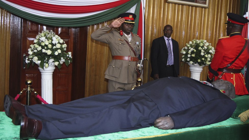 Офицер салютует перед телом покойного Даниэля Арапа Мои, второго президента Кении , лежащий в государстве в парламенте в Найроби, Кения