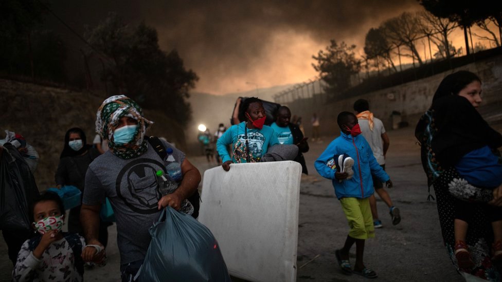 Refugees and migrants carrying their belongings flee a fire burning at the Moria camp on the island of Lesbos, Greece, 9 September 2021