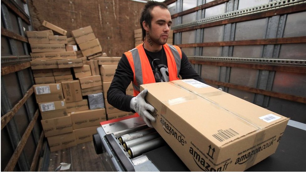 Рабочий Amazon загружает пакет в грузовик