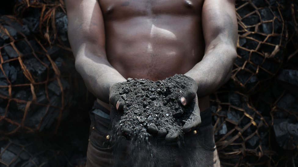 Un hombre muestra en sus manos un puñado de carbón descartado en un depósito en Dar es Salaam