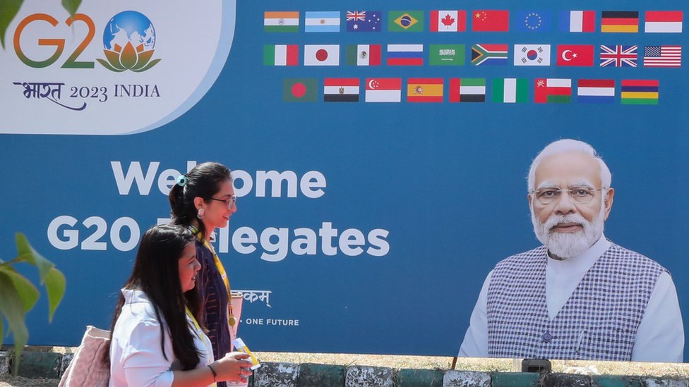 印度新德里街頭兩位女士走過配有總理莫迪肖像的G20峰會宣傳標語牌（8/9/2023）