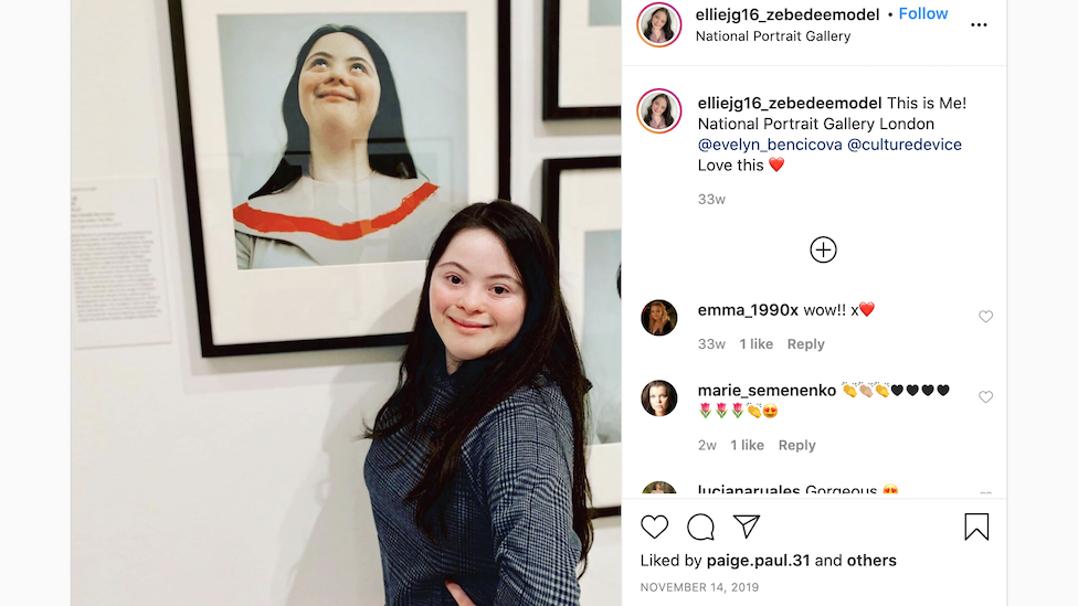 Ellie Goldstein posing next to a portrait of herself being exhibited at the National Portrait Gallery in London