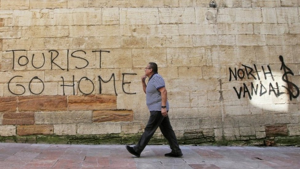 Мужчина проходит мимо надписи «Туристы идут домой» на стене рядом с мэрией в Овьедо, северная Испания,