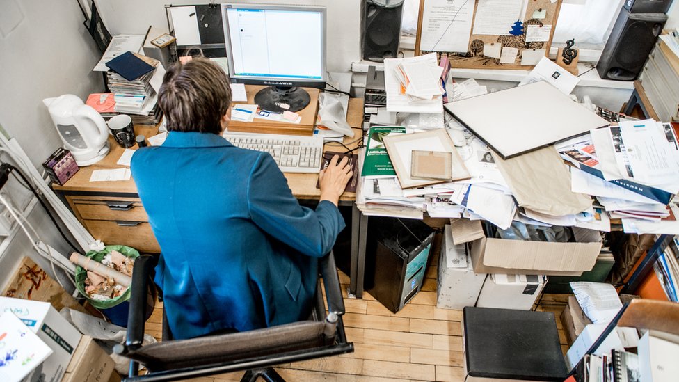Una persona sentada en un escritorio desordenado.