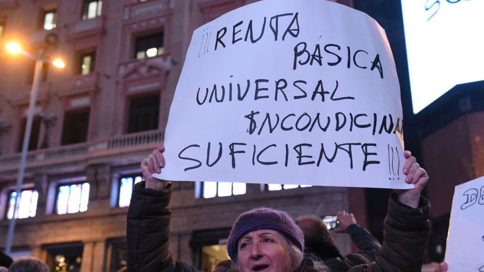 Persona en Madrid, España, con una pancarta pidiendo renta básica universal suficiente.