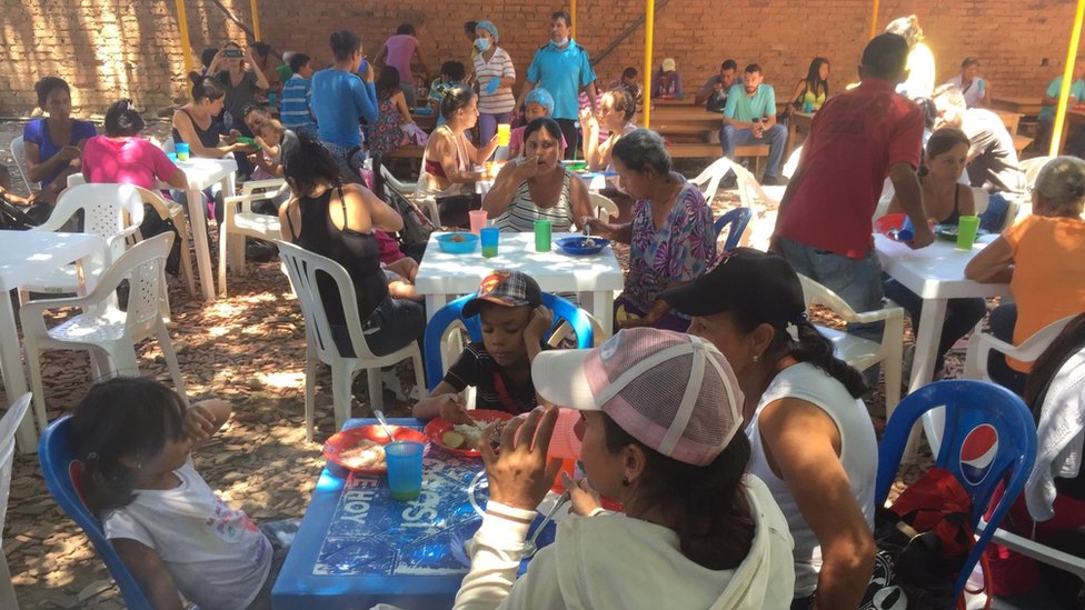 Люди сидят за пластиковыми столами и едят во дворе церкви в Кукуте
