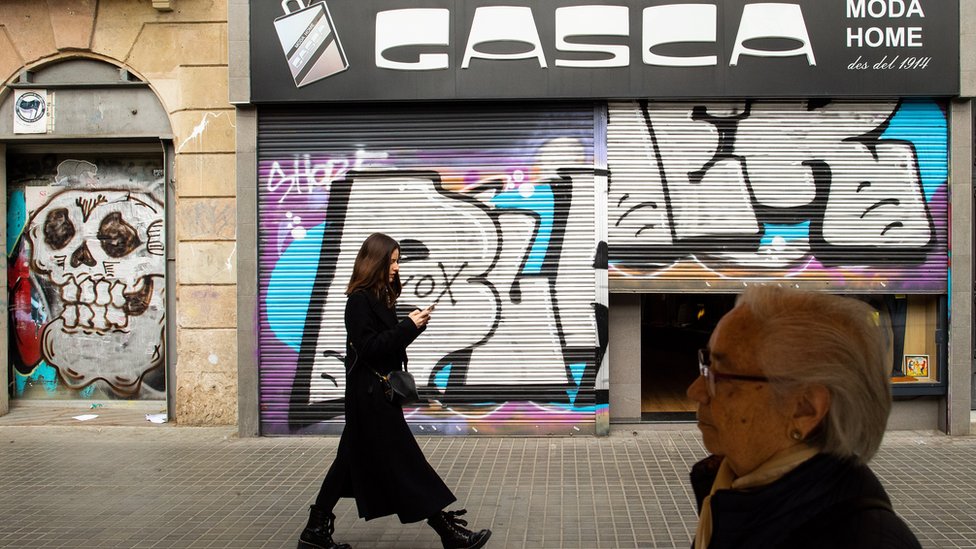 Представители общественности проходят мимо закрытого магазина, поскольку 14 марта 2020 года в Барселоне, Испания, вводятся новые меры против распространения коронавируса.