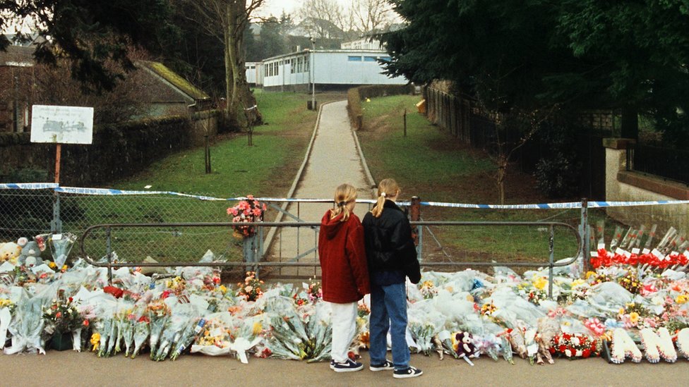 Дети рассматривают цветы, возложенные к воротам начальной школы Данблейн после стрельбы в 1996 году