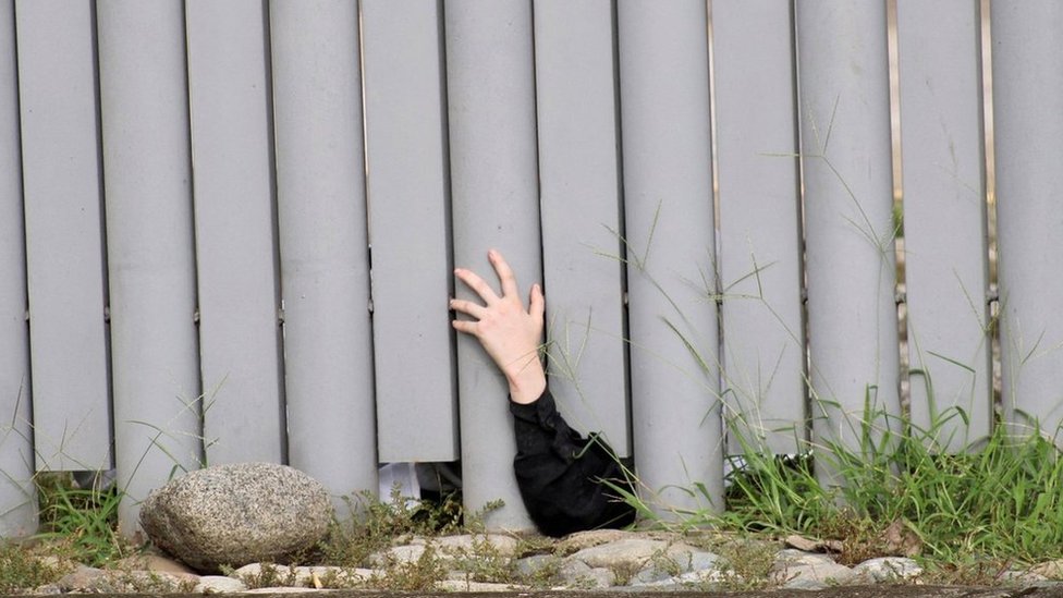 Un niño saca su mano por debajo de una cerca a manera de protesta.