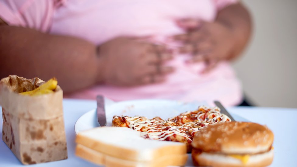 Un hombre con las manos en el estómago frente a comida grasosa