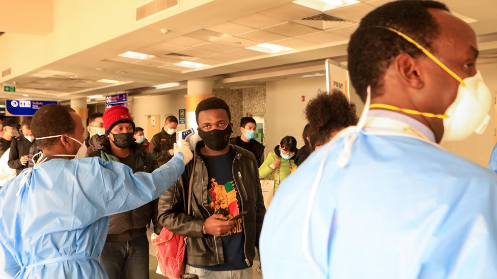 Пассажиры в масках стоят в очереди на досмотр после прибытия из Китая в международный аэропорт Джомо Кеньятта
