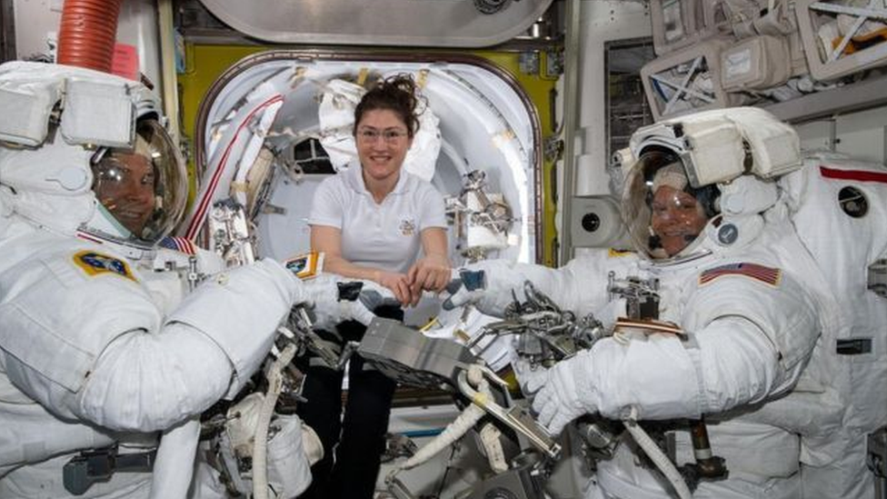 Üç astronot: İkisi uzay elbiseleriyle, kadın astronot normal giysisiyle