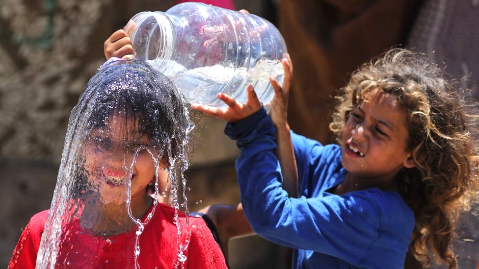 A Palestinian girl pours water over another girl, who is smiling