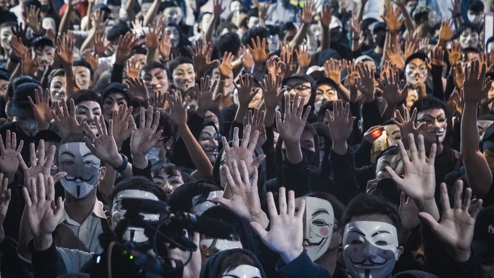 Митингующие приняли девиз: «Пять требований, не одним меньше!» и носила маски вопреки плану Кэрри Лэм призвать чрезвычайные полномочия колониальной эпохи, чтобы запретить маски