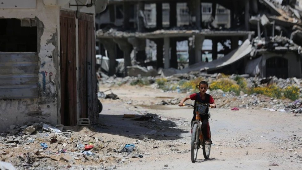 A boy on a bicycle with destroyed buildings behind him in the Az-Zaytoun neighbourhood in Gaza City