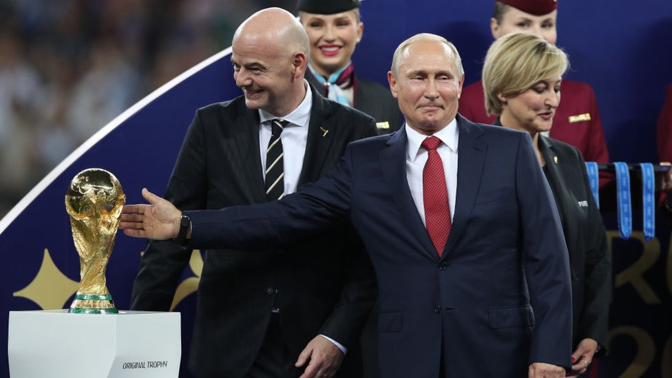 Putin gesturing at the World Cup trophy