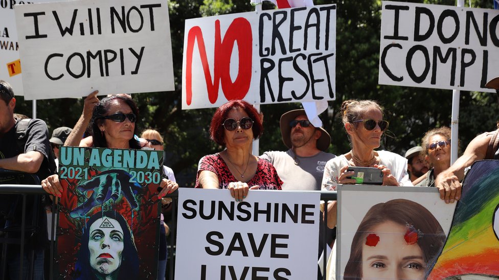 People hold placards protesting the United Nations and the "great reset" at a rally of conspiracy theorists and supporters of US President Donald Trump on January 14, 2021 in Wellington, New Zealand
