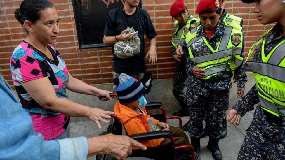 Mujer con empujando un menor en silla de ruedas frente al Hospital Infantil Dr, J M de los Ríos, en Caracas
