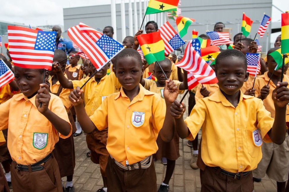 Дети машут флагами США и Ганы в честь первой леди США Мелании Трамп во время церемонии прибытия после приземления в международном аэропорту Котока в Аккре 2 октября 2018 года, когда она начинает свою недельную поездку в Африку для продвижения своей кампании «Будь лучшим».