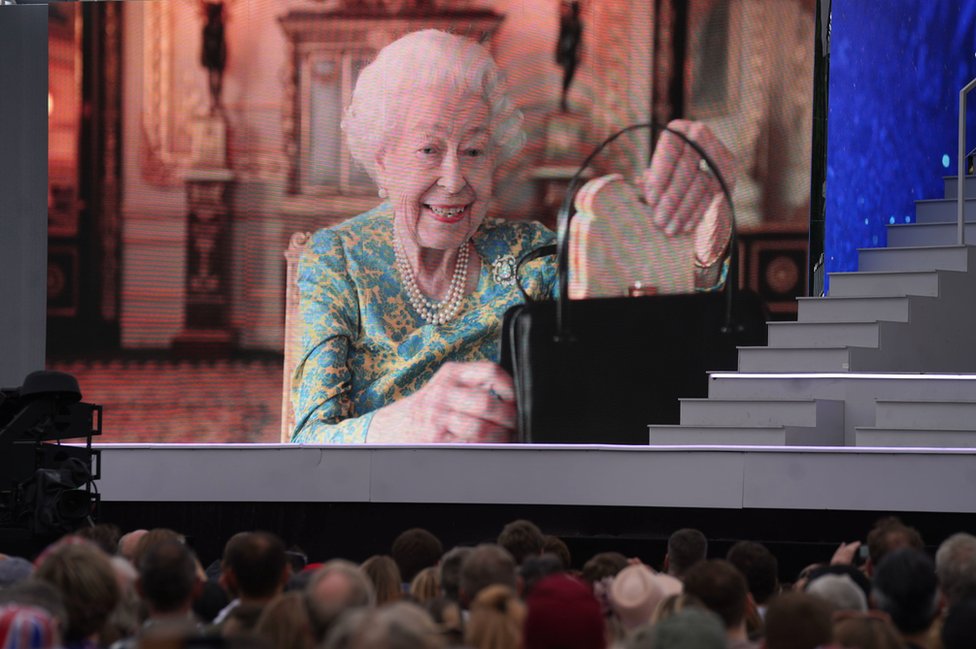 Kraljica vadi sendvič sa marmeladom iz ručne torbe, na velikom ekranu ispred Bakingemske palate