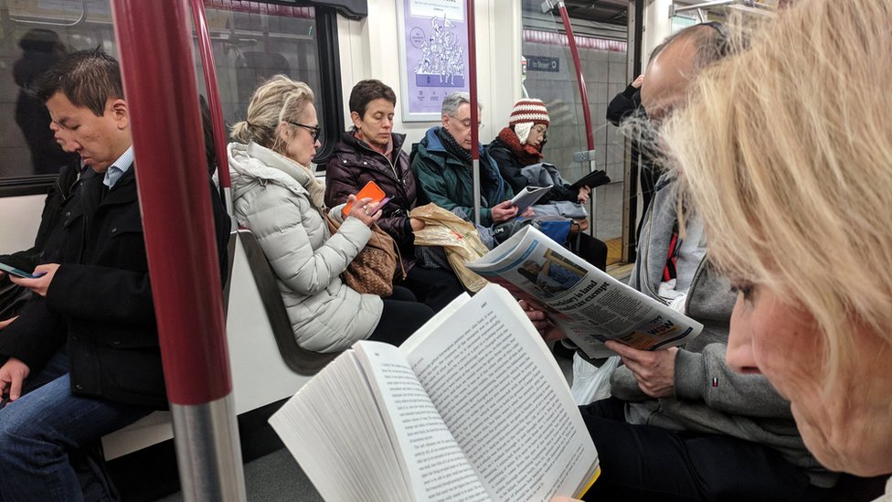 Утренние пассажиры читают, пока едут в метро TTC в Торонто, Онтарио, Канада