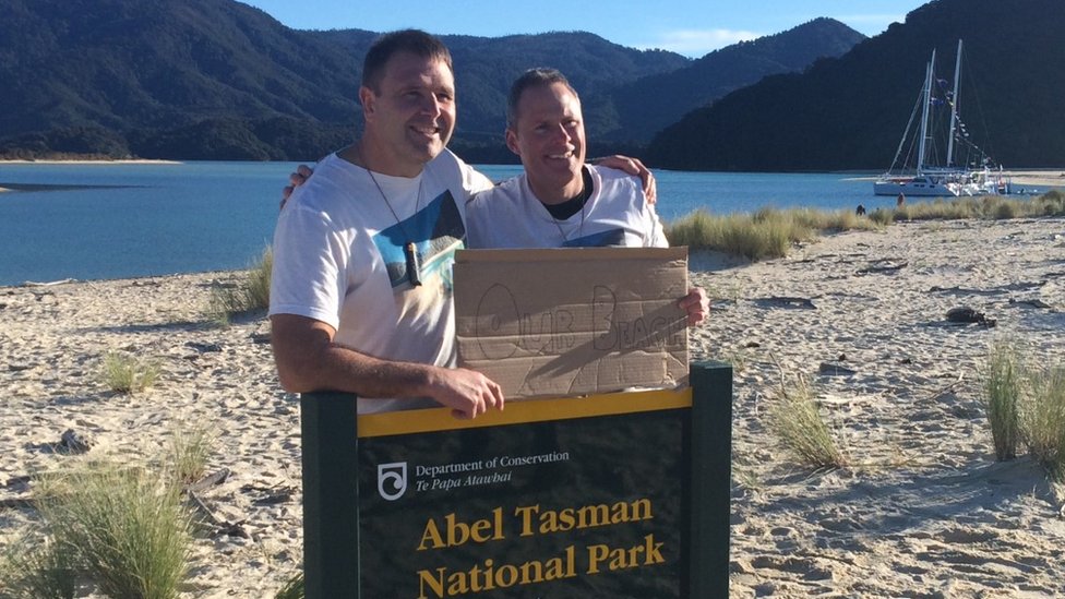 Два участника кампании держат табличку с надписью «Наш пляж», стоя на пляже в Новой Зеландии - 10 июля 2016 г.