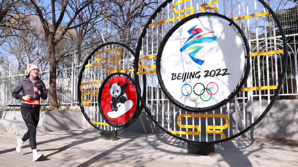 Woman runs in front of a sign for the Games in Beijing