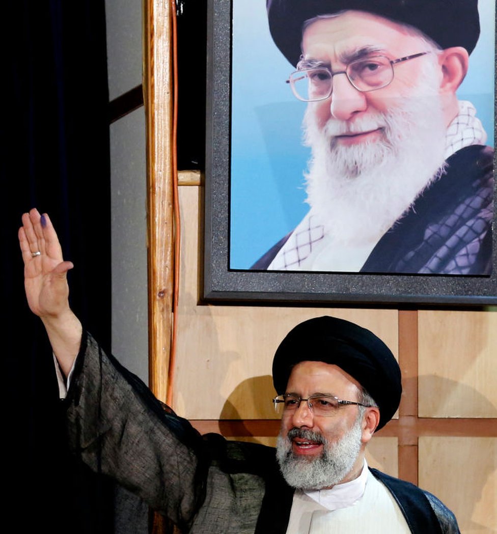 Raisi next to a painting of Ayatollah Khamenei.