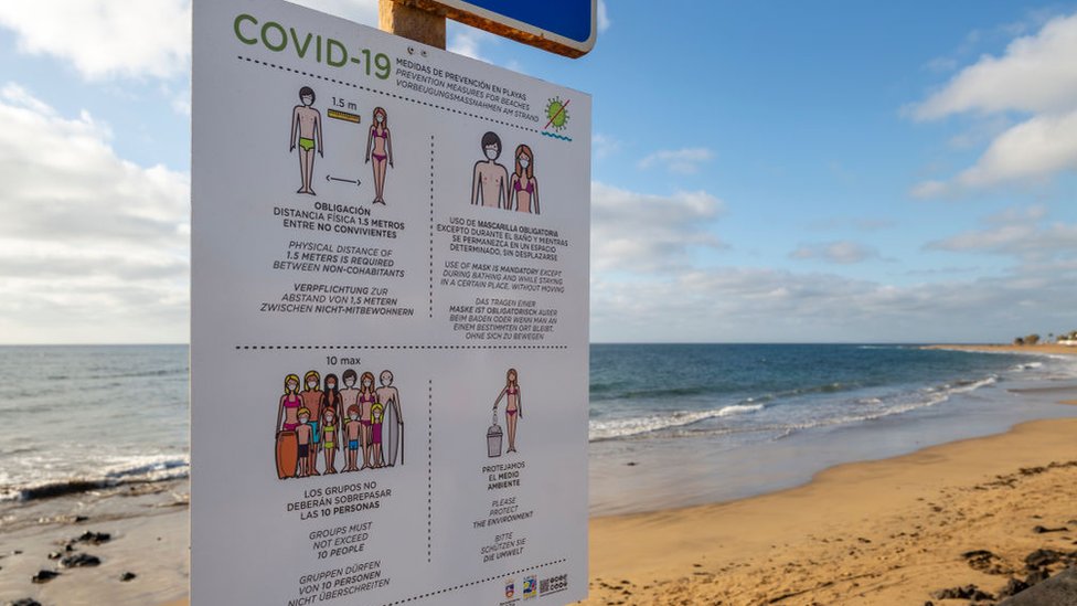Playa desolada en Lanzarote, España, con un cartel sobre las restricciones del covid