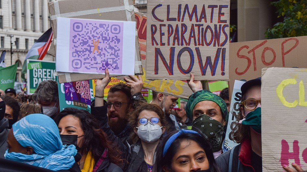 Manifestantes durante la COP26 con un cartel que pide reparaciones