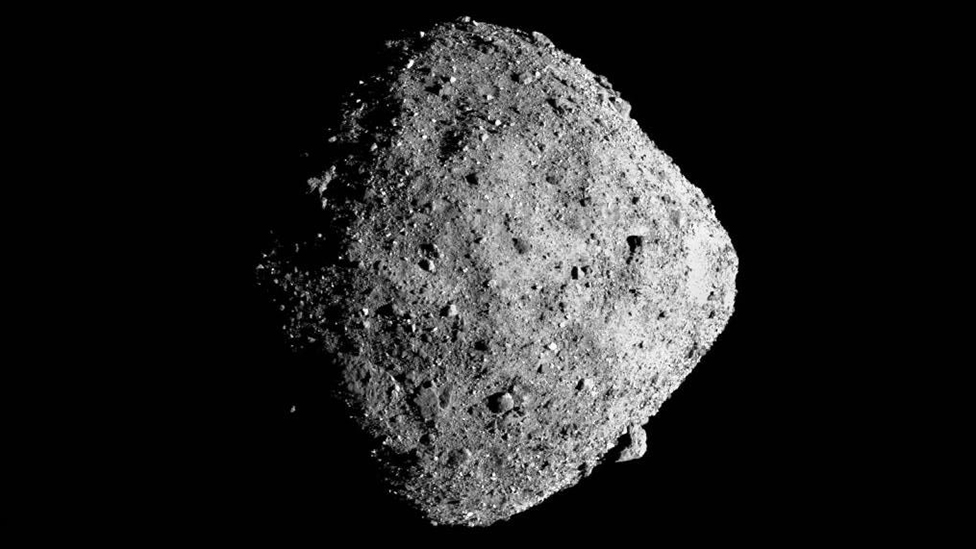 Imagem do Bennu no meio do espaço, com aparência de rocha e cor cinza