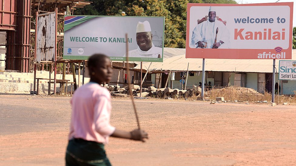 Человек проходит мимо досок с изображениями Яхьи Джамме в его родном городе Канилай, Гамбия - 22 января 2017 г.