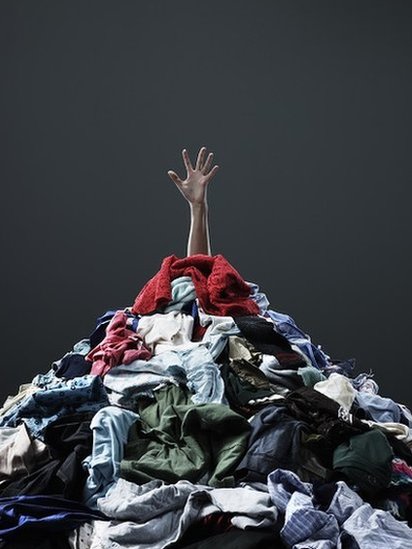 Una mano saliendo de una montaña de ropa para lavar