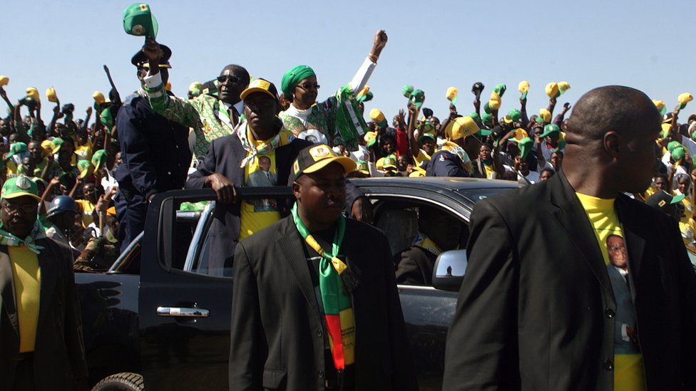 Роберт Мугабе (L в машине) машет рукой, когда он прибывает, чтобы обратиться к толпе, собравшейся во время предвыборного митинга, проведенного на стадионе Чибуку в Читунгвизе 16 июля 2013 года.