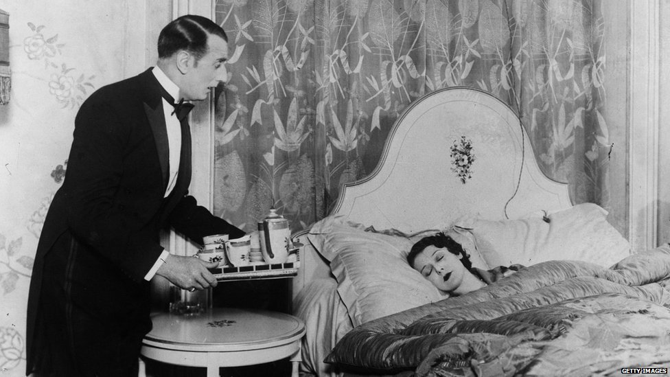Черно-белое фото дворецкого, приносящего напитки спящей женщине