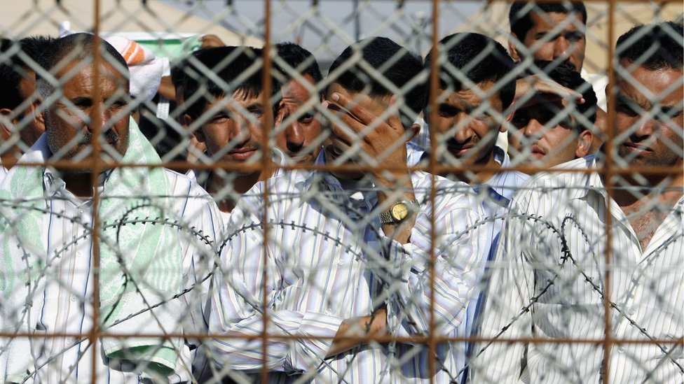 Заключенные тюрьмы Абу-Грейб недалеко от Багдада смотрят через забор безопасности