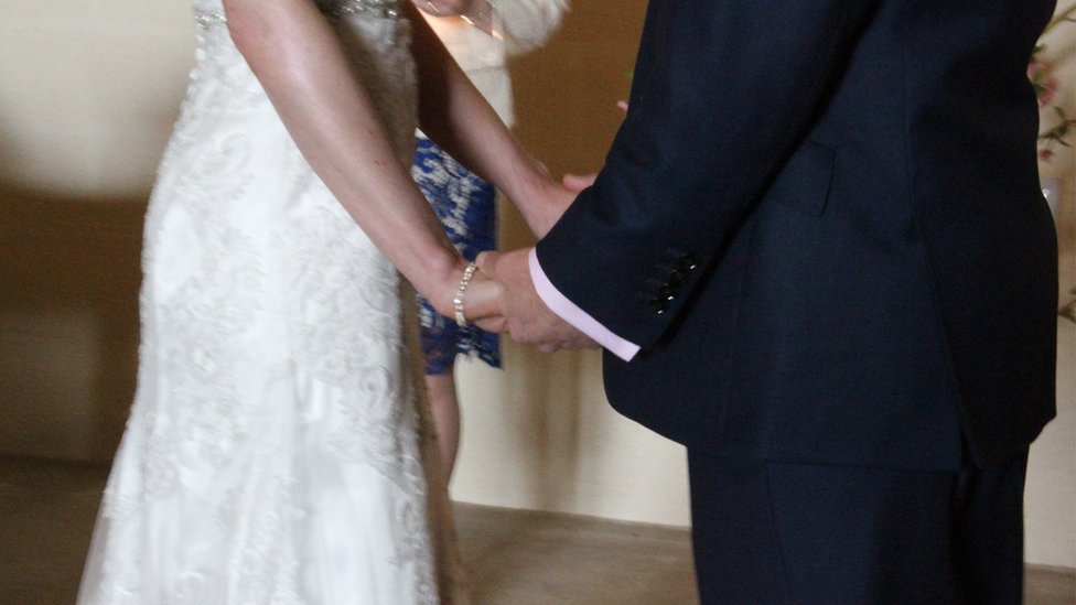 Неизвестная пара держится за руки на свадьбе