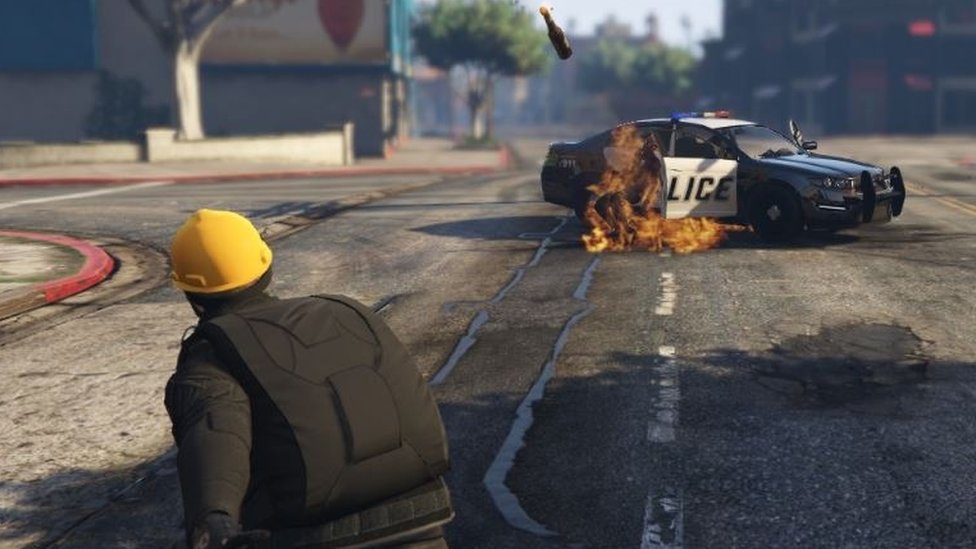 Протестующий бросает бомбу с бензином в полицейскую машину в GTA V.