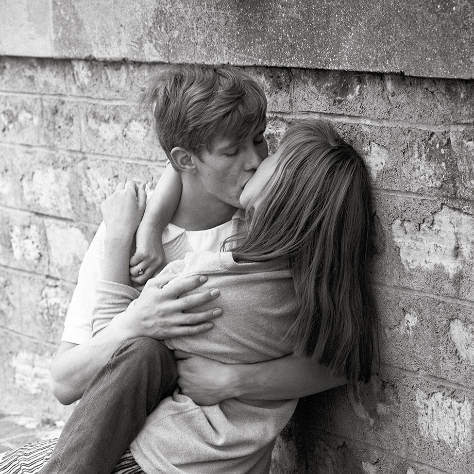Пара целуется, прислонившись к стене
