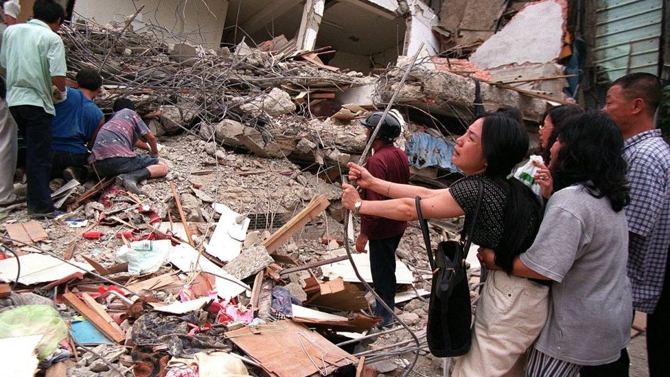 A woman weeps at the site of a collapsed building while workers dig through rubble to find survivors in the 1999 Chi-Chi earthquake