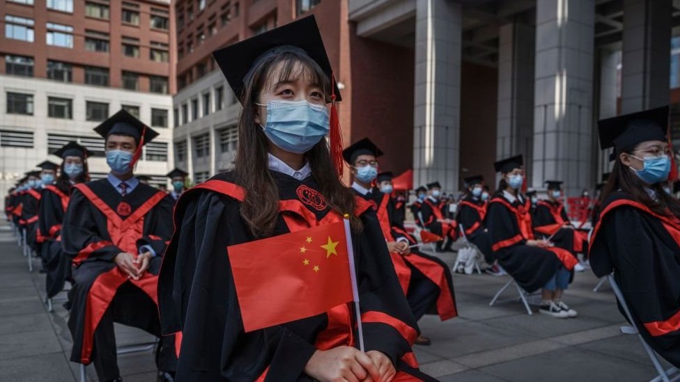 Students wear face masks and hold Chinese flags during a Beijing University open-air graduation ceremony