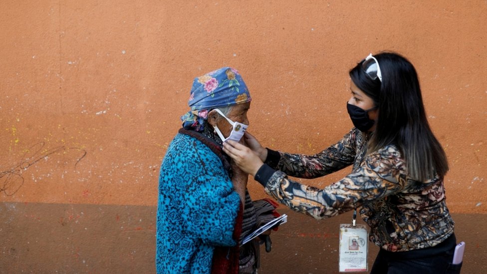 Муниципальный служащий надевает защитную маску на женщину на улице во время вспышки коронавирусной болезни (COVID-19) в Тотоникапан, Гватемала, 19 апреля 2020 г.