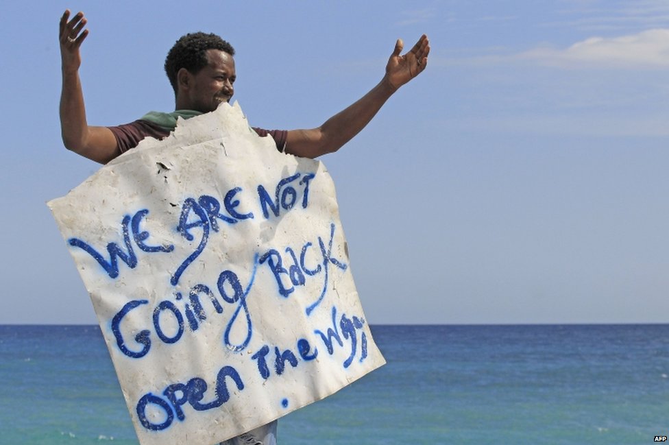 Мигрант держит плакат с надписью «Мы не вернемся назад», ожидая у моря в городе Вентимилья на французско-итальянской границе 15 июня 2015 г.