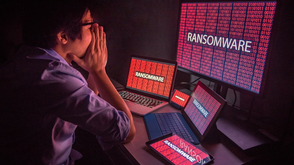 Existen sistemas diseñados para detectar comportamientos inusuales o softwares maliciosos en redes conectadas a internet. Hombre sentado frente a pantallas que dicen "ransomware".