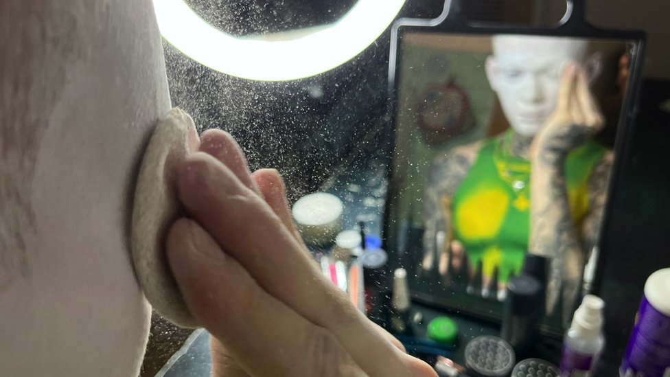 Danya aplicándose polvo blanco en la cara frente a un espejo.