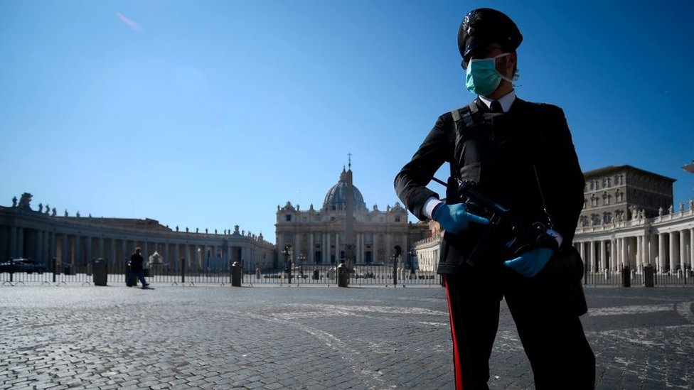 Вооруженный полицейский в маске патрулирует закрытую и заброшенную площадь Святого Петра в Ватикане