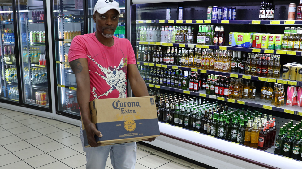 Покупатель несет коробку с алкоголем с надписью «Corona extra» в преддверии общенациональной изоляции на 21 день в Йоханнесбурге, Южная Африка, чтобы попытаться сдержать коронавирус