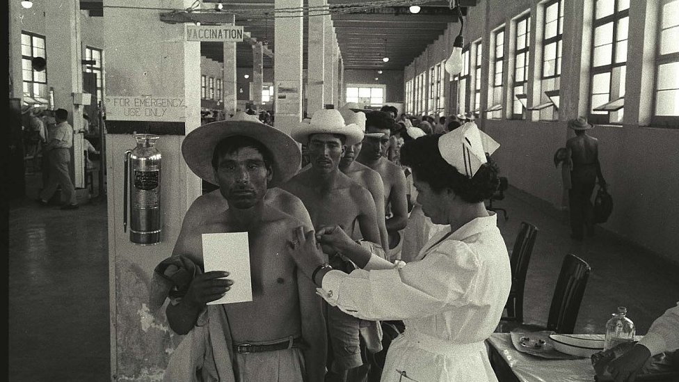 Un bracero es vacunado mientras otros esperan en la fila en el Centro de Procesamiento en Monterrey, México, en 1956.